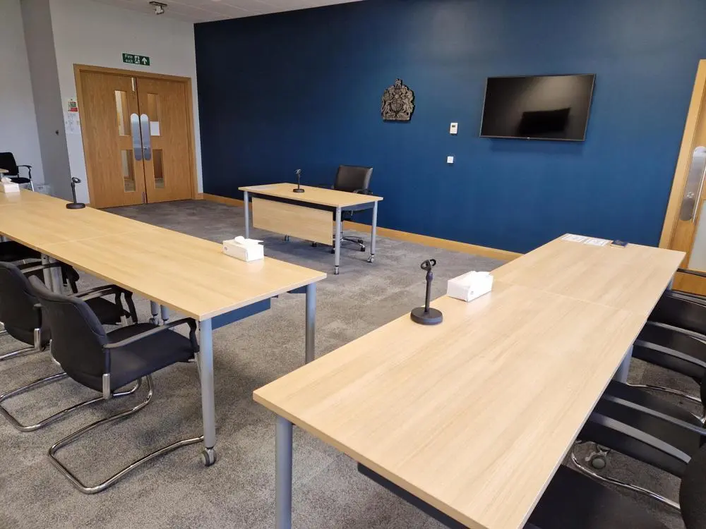 Beacon house small court room see from the back corner with tables arranged in a court style and a TV on the wall